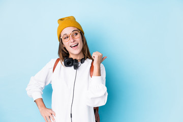 Young student woman isolated points with thumb finger away, laughing and carefree.