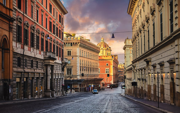 Fototapeta Rome, Italy. Deserted evening street of old town with road of paving stones and high houses. Picturesque landscape with sunset sky.