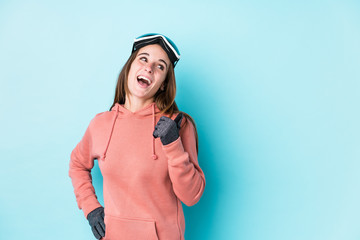 Young skier woman isolated points with thumb finger away, laughing and carefree.