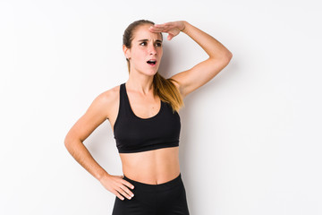 Young caucasian fitness woman posing in a white background looking far away keeping hand on forehead.