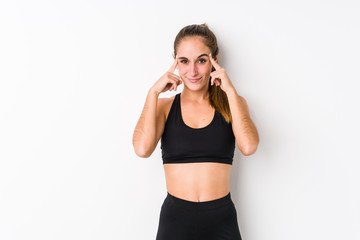 Young caucasian fitness woman posing in a white background focused on a task, keeping forefingers...