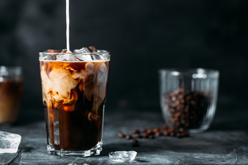 Milk Being Poured Into Iced Coffee on a dark table - obrazy, fototapety, plakaty