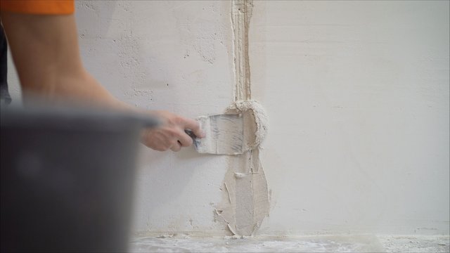 Worker using the trowel for plastering the concrete wall at the construction site. Making the smoothness and flat the surface of cement wall by wooden trowel. Labor day. 