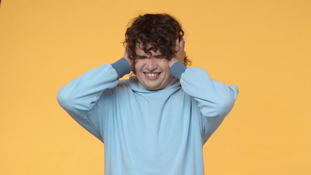 Stop please. Slow-motion fed up. distressed and depressed curly teen guy, shaking head in denial, close ears, holding hands on head, cringe upset, cant bear terrible noise anymore, hear awful sound