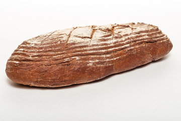 A whole loaf of fresh black rye bread with cuts from a knife on top of it and sprinkled with white flour isolated on a white background. Healthy eating concept.