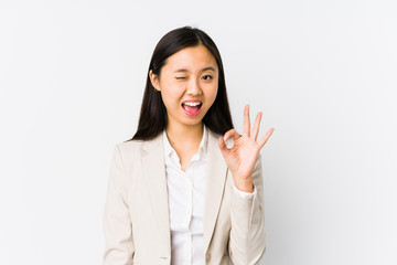 Young chinese business woman isolated winks an eye and holds an okay gesture with hand.