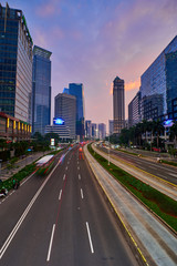 Fototapeta na wymiar Light trails on the busy traffic surrounded by Jakarta business office buildings with colorful sky