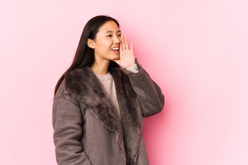 Young chinese woman wearing a coat isolated shouting and holding palm near opened mouth.