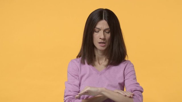 Slow-motion impatient and annoyed brunette female waiting for someone, looking at watch and breath-out bothered, eye-roll, hate not punctual people, awaiting over yellow background