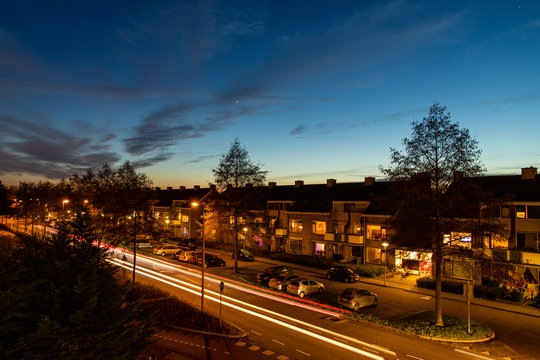 Moving cars in a street in Barendrecht city bij dusk. Red and white car lights under a black blue sunset dusk sky