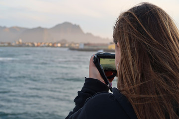 Young girl taking a picture to the landscape with a camera from a boat.