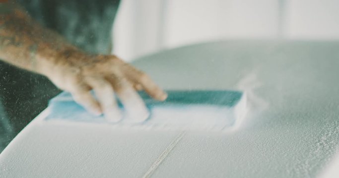 Close up shot of a surfboard shaper's hand sanding a new surfboard, experienced craftsman surfboard shaper shaping a new board