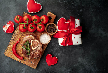 grilled steak, with tomatoes and spices with various red hearts on a stone background. Valentine's dinner concept