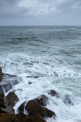 A huge ocean waves breaking on the coastal cliffs in at the cloudy stormy day. Breathtaking romantic seascape of ocean coastline.