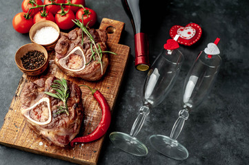 two grilled steaks, with tomatoes and spices with a bottle of wine and glasses, various red hearts on a stone background. dinner for two on valentine's day