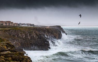 A huge ocean waves breaking on the coastal cliffs in at the cloudy stormy day. Breathtaking romantic seascape of ocean coastline. Peniche, Portugal.