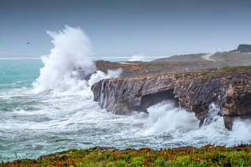 A huge ocean waves breaking on the coastal cliffs in at the cloudy stormy day. Breathtaking romantic seascape of ocean coastline.