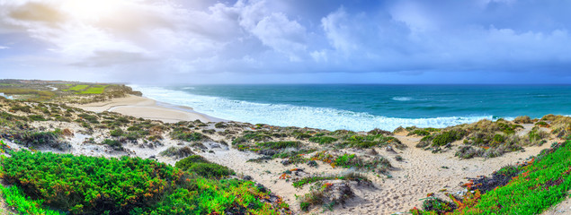 A ocean waves on the beautiful sand beach in at the cloudy stormy day. Breathtaking romantic panoramic seascape of ocean coastline. Praia d'el rey near Obidos Lagoon. Portugal.