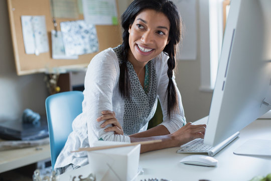Mid adult female jewelry artist smiling while looking away at computer desk