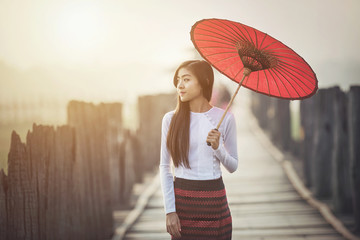 Burmese women in Burmese Traditional dress with red umbrella on U bein bridge Mandalay, Myanmar.