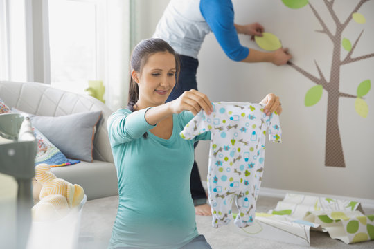 Pregnant Woman Holding Onesie In Nursery