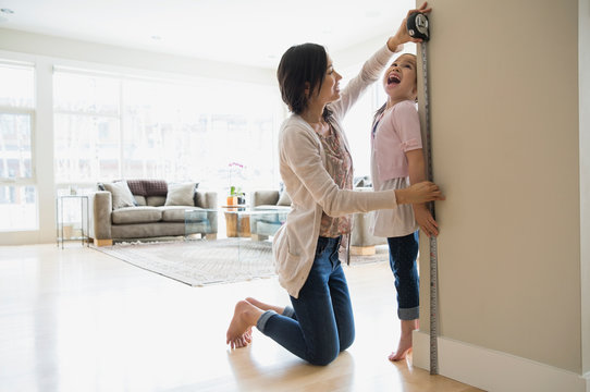Mother measuring daughters height in living room
