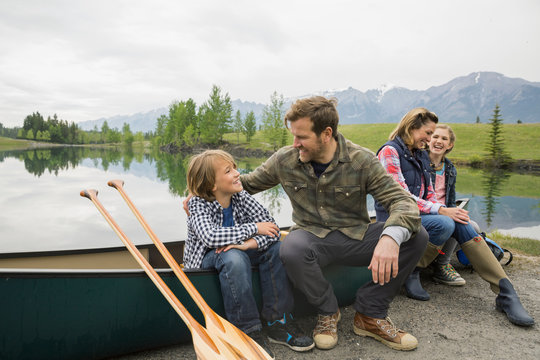 Family sitting by canoe by still lake