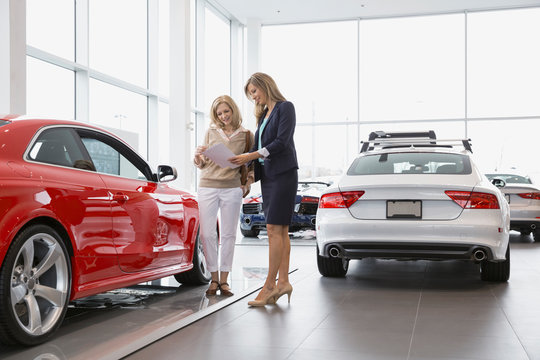 Saleswoman showing woman brochure in car dealership showroom