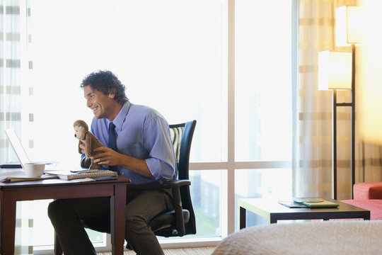 Man In Hotel Room On Business Trip Video Chatting With Kids At Home