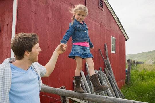 Father helping daughter balance on rural fence