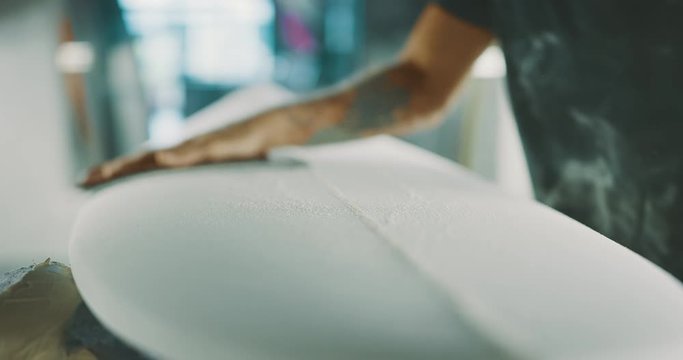 Surfboard shaper carefully sanding a new surfboard, skilled craftsman working on a new design in his workshop
