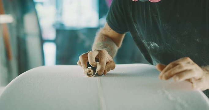 Surfboard shaper using a planer tool to shave a surfboard stringer, skilled craftsman working with his hands shaping a new surfboard with precision