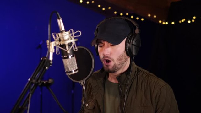 4K: Male Singer / Popstar recording an Album in the studio - He sings into the Microphone with headphones & Baseball Cap on