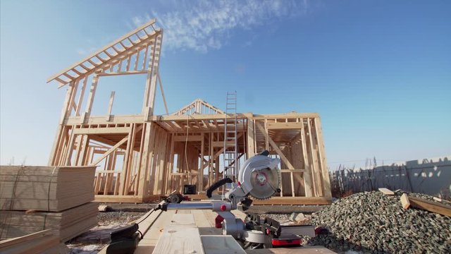 Camera is moving backward, zooming out view of circular saw and wooden frame house under construction on the background
