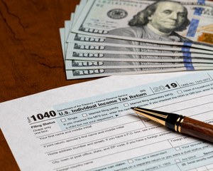 1040 individual income tax return form 2019 with ballpoint pen 100 dollar bills. Concept of filing taxes, payment, refund, and April 15, 2020 deadline date