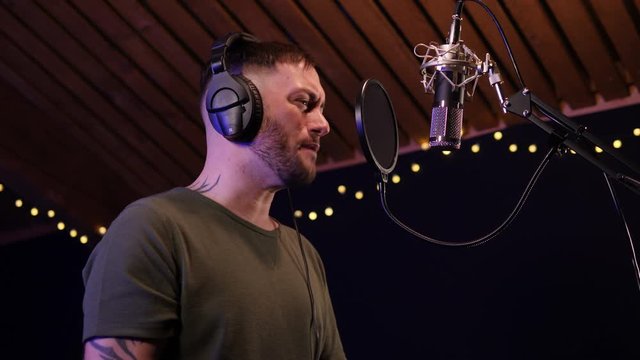 Male Singer / Popstar recording an Album in the studio - He sings into the Microphone with headphones on. Tilt Up