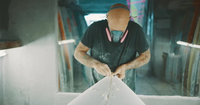 Surfboard shaper using a planer tool to shave a surfboard stringer, skilled craftsman working with his hands shaping a new surfboard