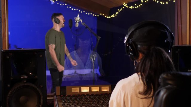 Male Singer / Popstar recording an Album in the studio - With female Sound Engineer in front mixing the track
