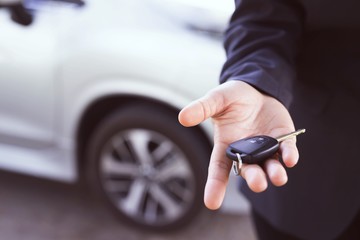 The car salesman shows the car keys to the customers at the showroom.