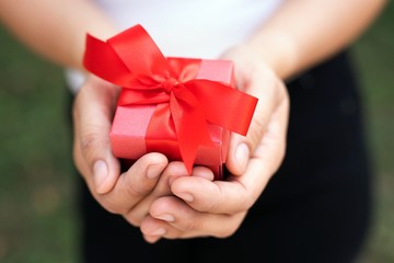 Red bow gift box in woman's hand for lover on birthday, new year, valentines day