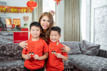 Asian mother with two son holding ang pao smiling looking at camera.Asian Chinese family celebrates...