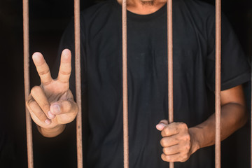 hand man lift two fingers and hold steel in jail on black background.concept for prisoner,fight in...