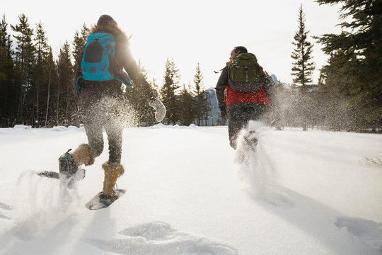 Friends running in snowshoes in snowy field