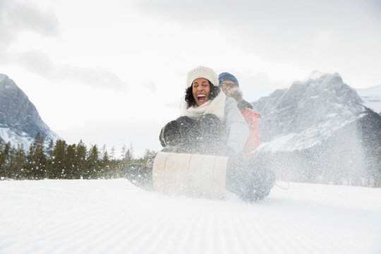 Exuberant couple sledding in snowy field