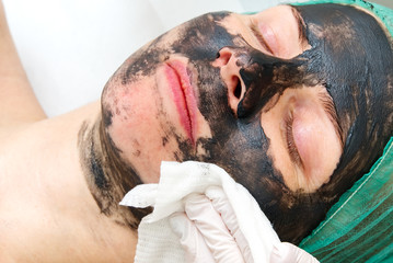 Beautician washes off a natural moisturizing mask on the face of a young beautiful woman. Black bamboo mask. Close up photo