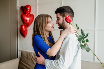 man and woman with red rose at home with heart shaped balloons