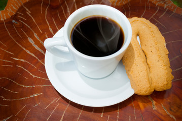  Cup of coffee accompanied by toast or cookie called Herraje, typical tablecloth on wooden table.