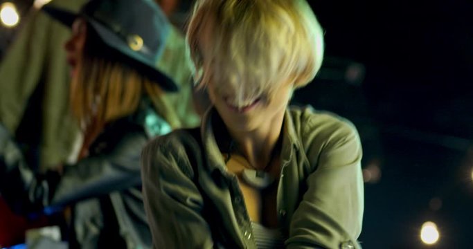 Close up of the young blonde Caucasian woman with short hair dancing a lot and moving in the rhythm of music at the night party outdoor.