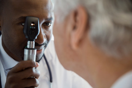 Doctor checking senior mans eyes with otoscope