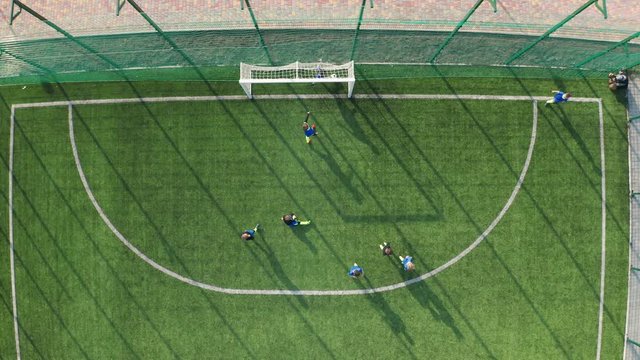 Top view of preteen soccer players scoring goal after masterfully kicked corner while playing football on green pitch. Drone shot of children's football team working out corner kick during soccer game